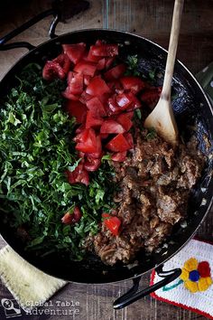 a skillet filled with meat and vegetables on top of a wooden table next to a cloth