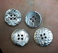 four silver buttons in the palm of someone's hand, some with holes on them