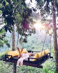 a woman laying in a hammock suspended between two trees with yellow pillows on it