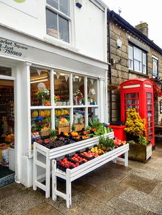 a fruit and vegetable stand in front of a building with a red phone booth next to it