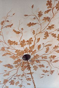 the ceiling is painted with gold leaves and branches on white walls, along with a chandelier