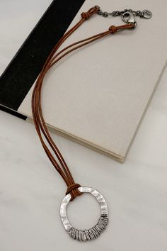 Expertly crafted with double leather cords and a hammered wire wrapped pendant, this rustic necklace adds a touch of vintage charm to any outfit. The unique design and high-quality materials make it a timeless accessory that will elevate your style. Details:- Genuine Leather Cord- Adjustable by 2.75"- Simple Hammered Oval Pendant- Handmade at JFY Dimensions:- Approx. 18" Length- Extendable by 2.75"- Pendant Diameter: 1.75" Rustic Necklace, Timeless Accessories, Oval Pendant, Wrapped Pendant, Wire Wrapped Pendant, Leather Cord, Vintage Accessories, Vintage Charms, Wire Wrapped