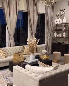 a living room filled with lots of furniture next to large windows and gold accents on the walls