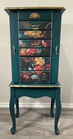 an old dresser with flowers painted on the drawers and gold trimmings, sits against a white wall