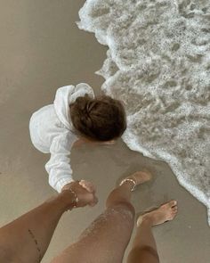 two people standing on the beach with their feet in the water and one is wearing a white shirt