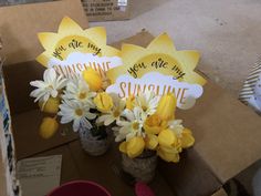 two vases filled with yellow and white flowers on top of a cardboard carton