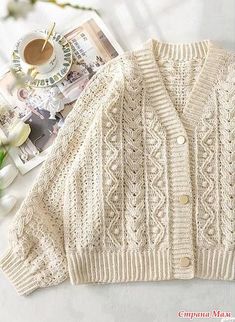 a white knitted cardigan sweater next to a cup of coffee on a table