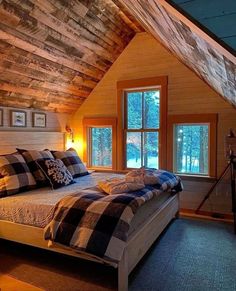 a bed in a room with wooden walls and ceiling, along with two windows that look out onto the woods