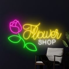 a neon sign that says flower shop next to a chair with a plant in it