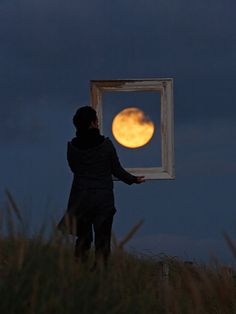 a person standing on top of a grass covered hill next to a window with the moon in it