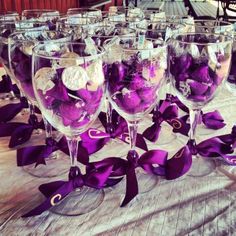 several wine glasses filled with purple candies on a table cloth covered tablecloth and ribbon