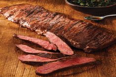 some steaks are on a wooden table next to a bowl of greens and a spoon