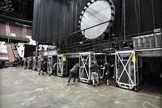 several people are standing around in front of a large clock on the stage at a concert