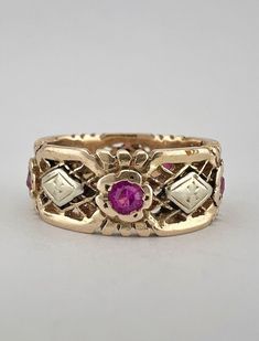 a gold ring with pink stones on the sides and an ornate design in the middle