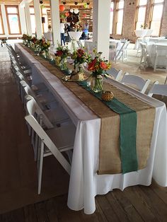 a long table is set up with white chairs and green runneres on the tables