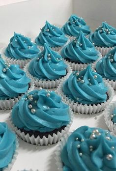 cupcakes with blue frosting and pearls on them are arranged in a box