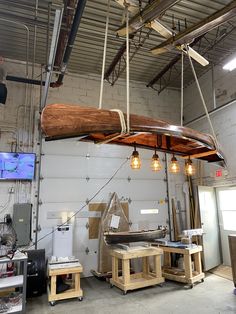 a large wooden object suspended from the ceiling in a warehouse with several tables and stools