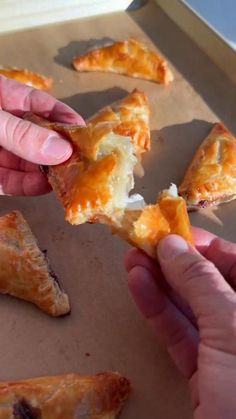 two hands holding pieces of pizza in front of each other on top of a baking sheet