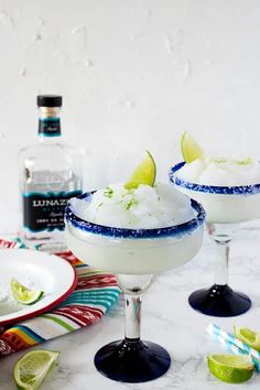 two margarita cocktails with lime slices on the rim, and a bottle of vodka in the background