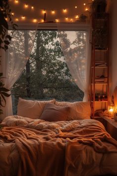 an unmade bed in front of a window with fairy lights hanging from the ceiling