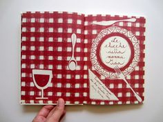 a hand holding an open red and white checkered cookbook with utensils on it