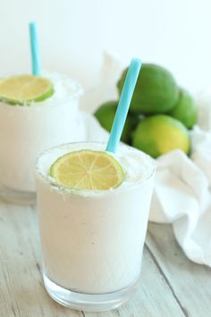 two glasses filled with drinks sitting on top of a wooden table next to limes