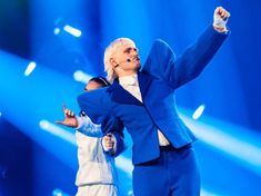 two people dressed in blue and white performing on stage with one holding his arm up