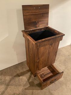 a wooden trash can sitting on top of a cement floor next to a white wall