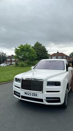 a white rolls royce parked on the side of a road with people standing next to it