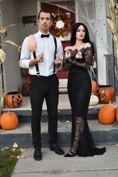 a man and woman dressed up for halloween standing in front of a house with pumpkins