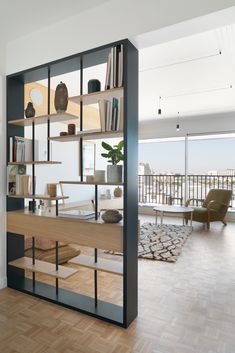 a living room filled with furniture next to a large glass wall mounted book shelf on top of a hard wood floor