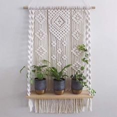 three potted plants sit on a shelf in front of a macrame wall hanging