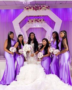 a group of women standing next to each other in front of a purple wall and chandelier