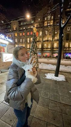 a woman holding up a small christmas tree on the sidewalk in front of a building