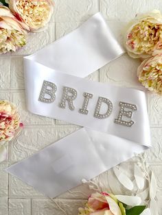 the bride sash is white with silver sequins on it and sits next to flowers