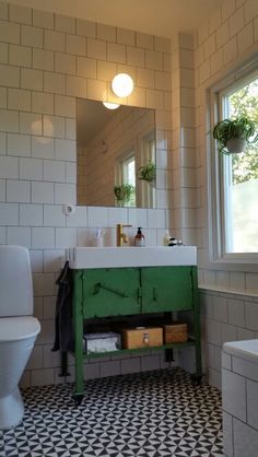 a white toilet sitting next to a green sink in a bathroom under a window with potted plants on it