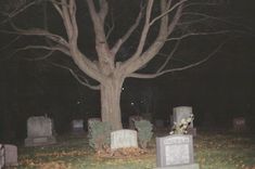 an old cemetery at night with tombstones in the foreground and a large tree behind it