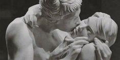 a black and white photo of a man kissing a woman's face in front of a statue