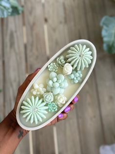 a person holding a bowl with flowers in it on a wooden floor next to a plant