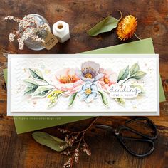 a card with flowers and leaves on it next to scissors, thread and spools