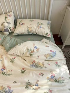 an unmade bed with white and green sheets, pillows and stuffed animals on it