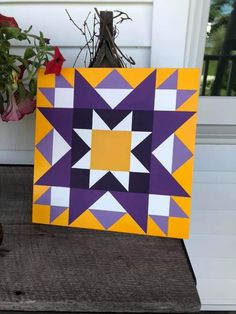 a purple and yellow quilt sitting on top of a wooden table next to a potted plant