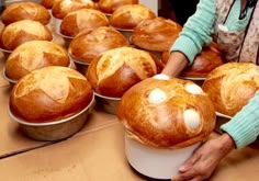 a woman holding a bucket full of breads on top of a wooden table next to other muffins