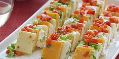 many different types of appetizers are arranged on a white platter with wine glasses in the background