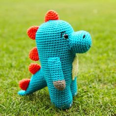 a crocheted blue and orange dinosaur sitting in the grass