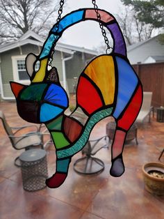 a stained glass cat hanging from a chain on a patio with chairs and tables in the background