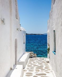 an alley way leading to the ocean with white buildings and blue water in the background