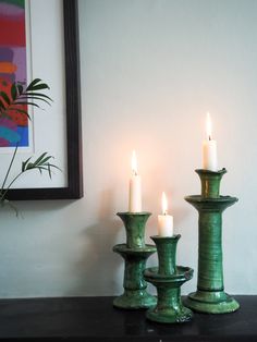 three lit candles sitting on top of a black table next to a framed painting and potted plant