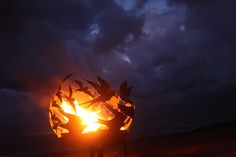 a fire pit sitting on top of a sandy beach under a cloudy blue sky at night