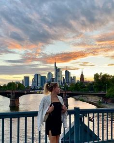 a woman standing on top of a bridge next to a river under a cloudy sky